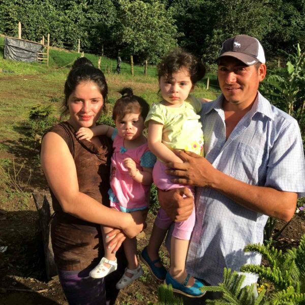 Familienfoto der Farmerfamilie Jose & Emma in Nicaragua. Die jungen Eltern halten jeweils eines ihrer beiden Kinder auf dem Arm.Im Hintergrund ist das Farmgelände zu sehen.